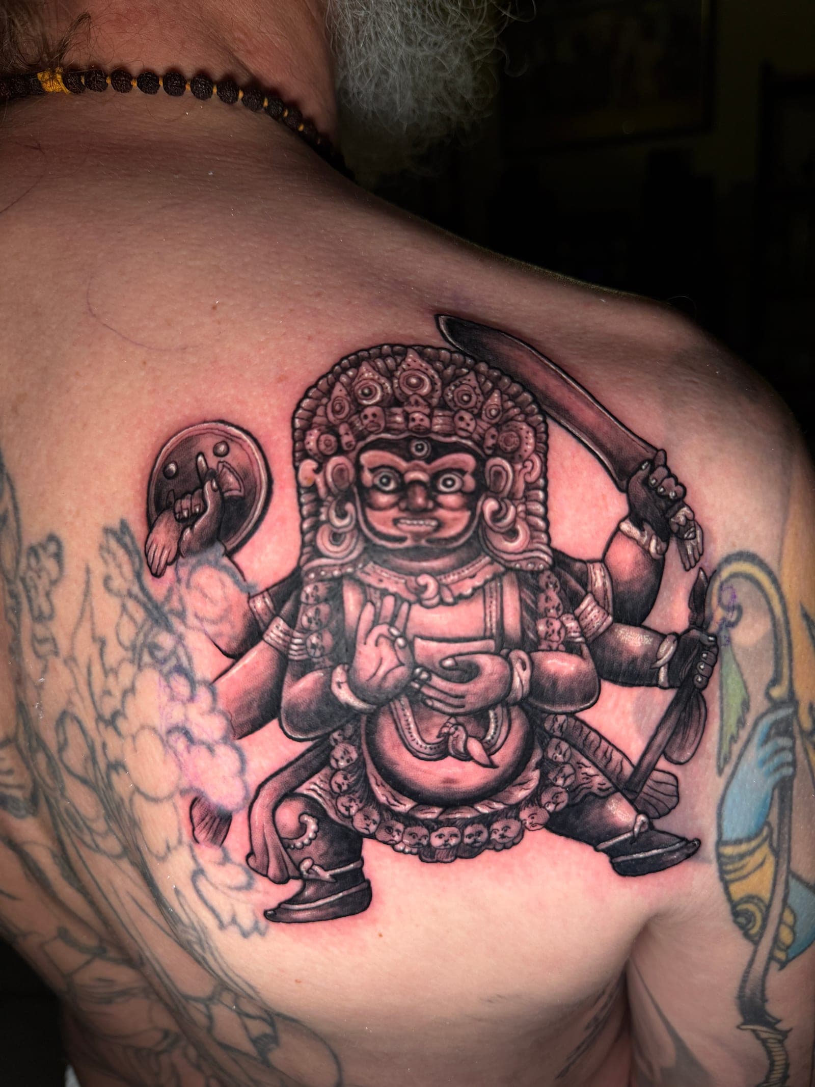 Traditional Himalayan wrathful deity back tattoo with skull crown and trident, done in Pokhara