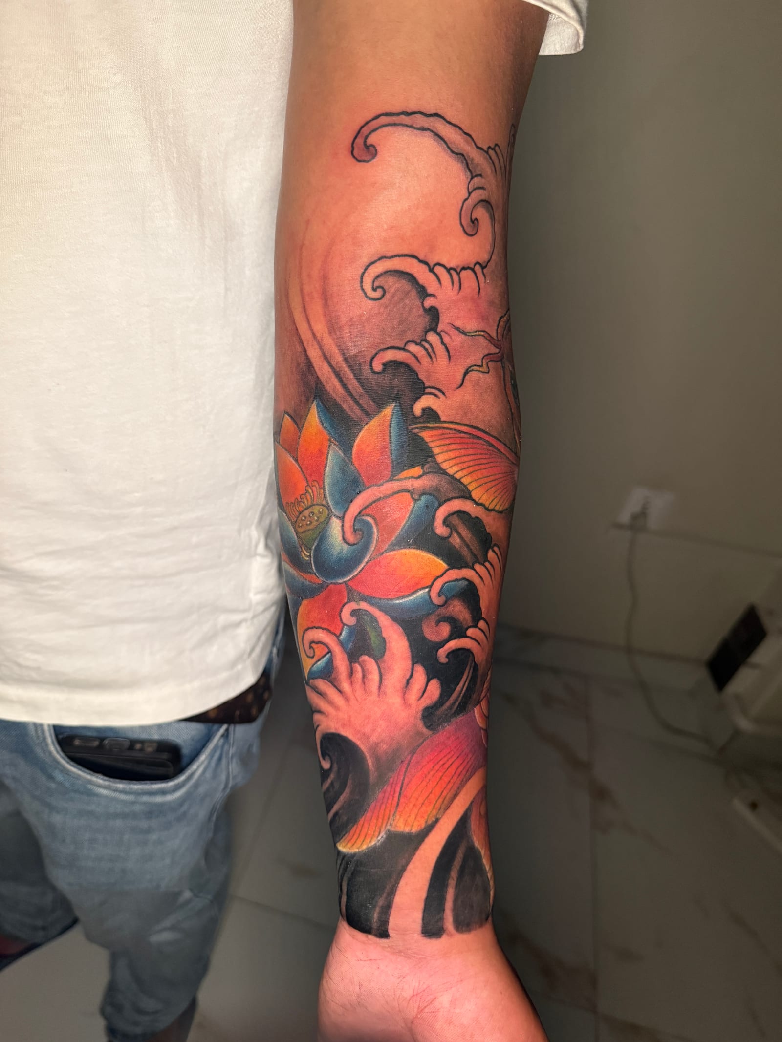 Bold color lotus and wave tattoo by Master Ananda in Pokhara, compared with blackwork styles at the studio